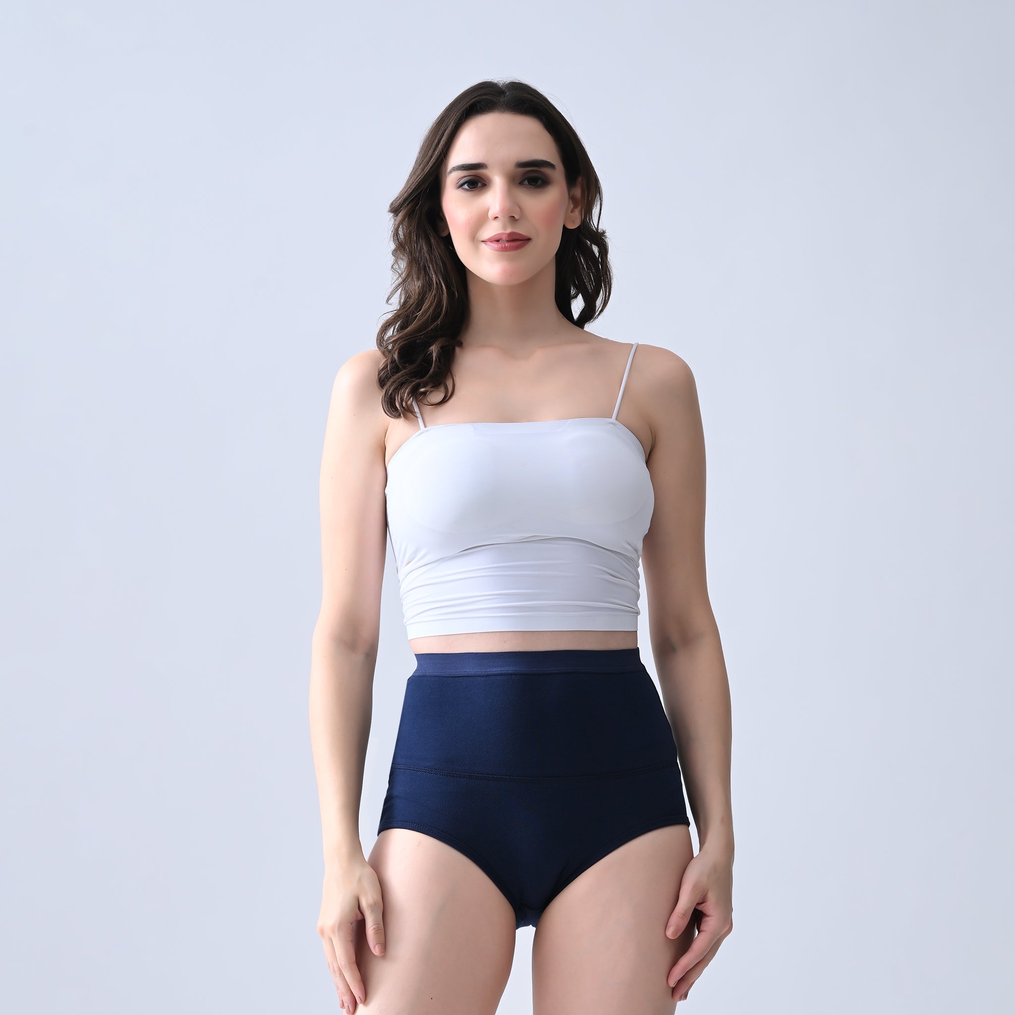 Woman wearing a white top and Woomly's Leakproof navy high-waisted shorts on a light gray background
